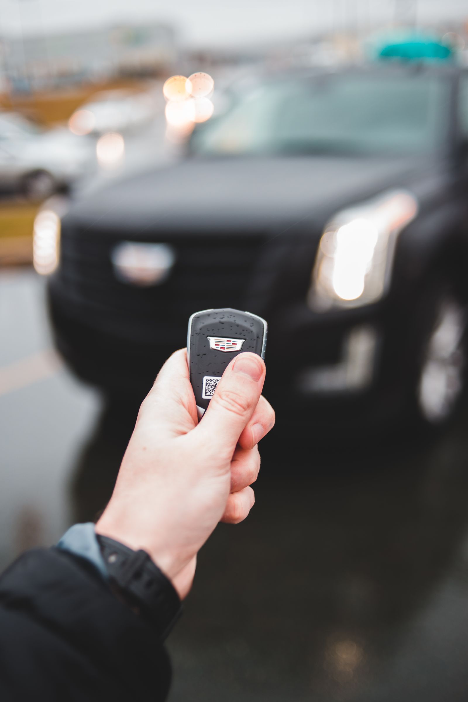 Hand holding a car key fob remote in front of a vehicle